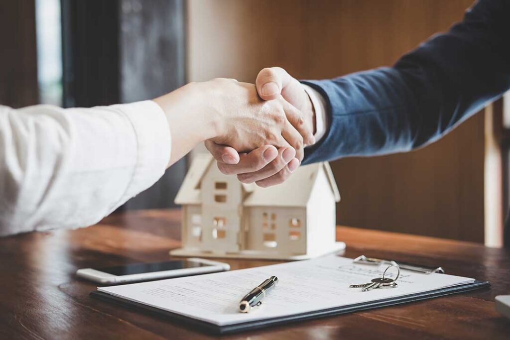 A couple reviews documents with a real estate agent around a kitchen table, surrounded by paperwork and coffee mugs.